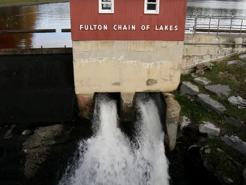 Water rushing through the Old Forge Dam under the Fulton Chain of Lakes sign